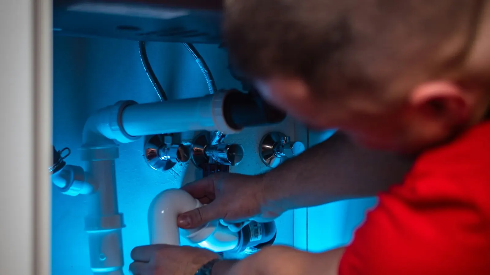 Technician working on plumbing inside a kitchen cabinet