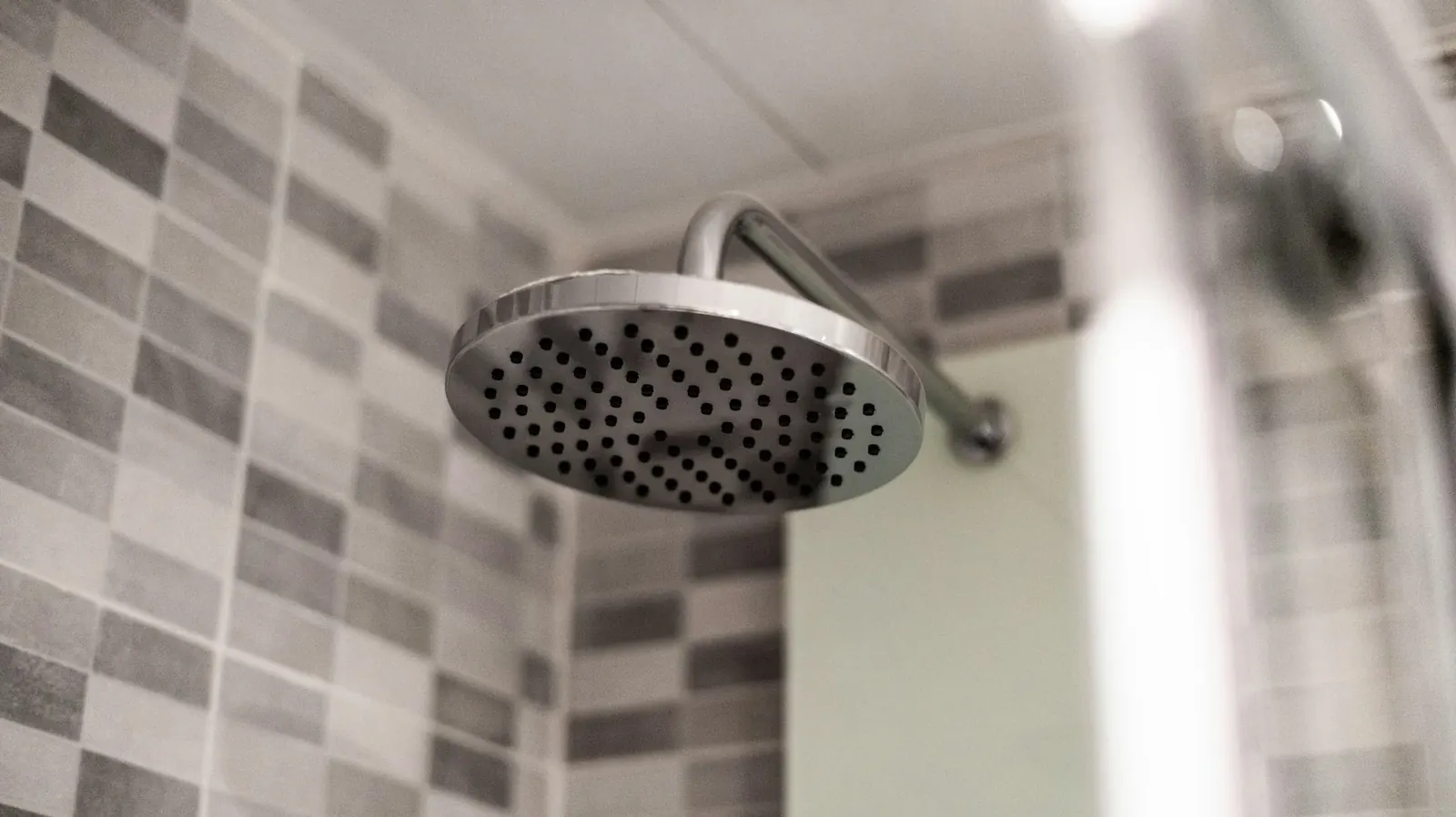 Shower head running in a tiled bathroom