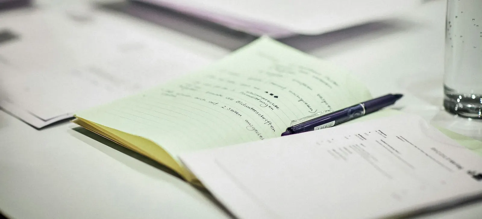 Paperwork and a pen beside a glass of water