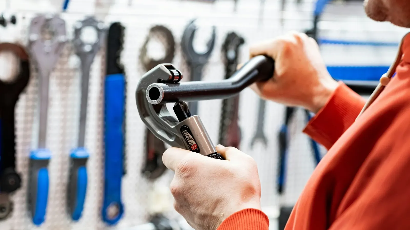 Hands holding a pipe wrench in front of a tool wall